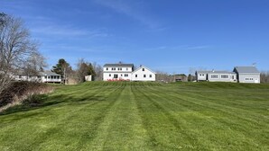 A large, white two-story house with a well-maintained lawn and a clear blue sky. - Oceanfront mid-coast Maine Getaway! (Stockton Springs)