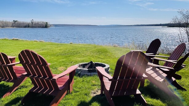 A lakeside view with three Adirondack chairs facing a fire pit. - Oceanfront mid-coast Maine Getaway! (Stockton Springs)