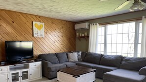 A living room with a television, grey sofas, a wooden coffee table, and a ceiling fan. - Oceanfront mid-coast Maine Getaway! (Stockton Springs)