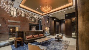 Un hall d’entrée moderne avec une cheminée, des canapés en cuir, un lustre et une moquette bleue.