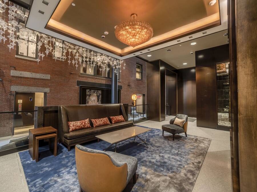 A modern lobby with a fireplace, leather sofas, a chandelier, and a blue carpet.