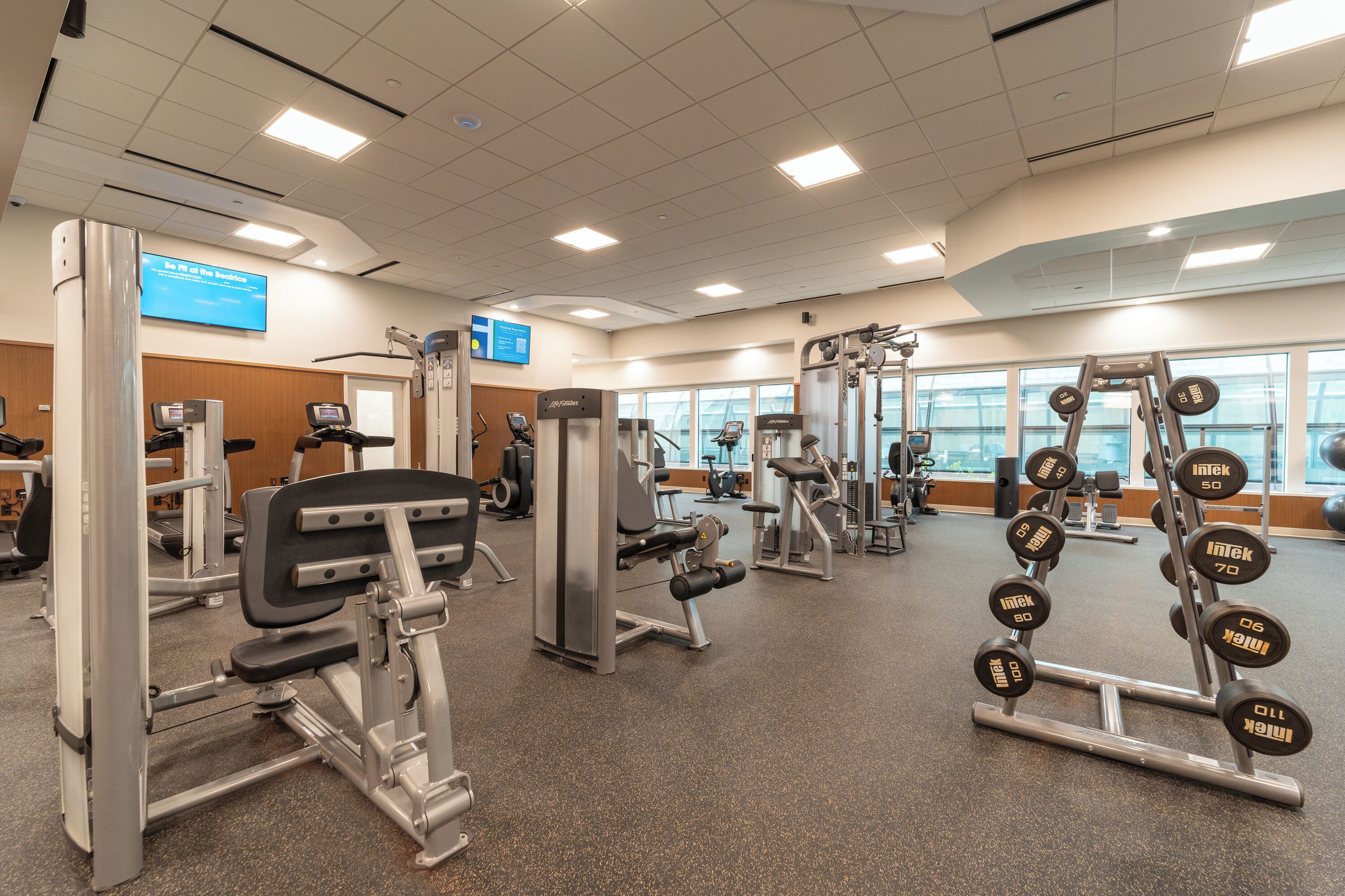 A gym with various exercise machines, weight stacks, and a digital screen displaying information.