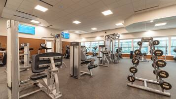 A gym with various exercise machines, weight stacks, and a digital screen displaying information.