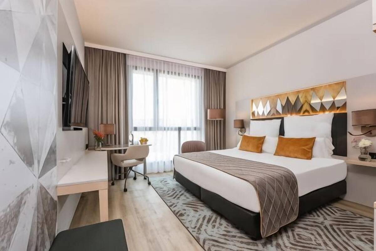 Une chambre d’hôtel équipée d’un lit, d’un bureau, d’une chaise, d’une télévision et de grandes fenêtres.