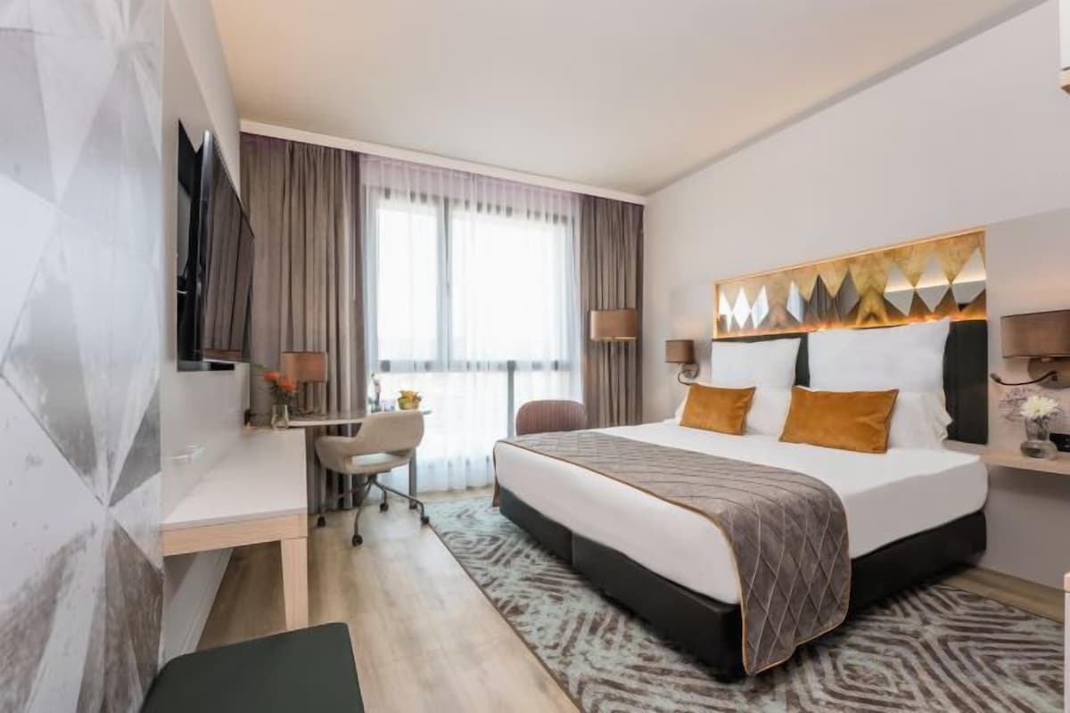 A hotel room with a bed, desk, chair, and a television.