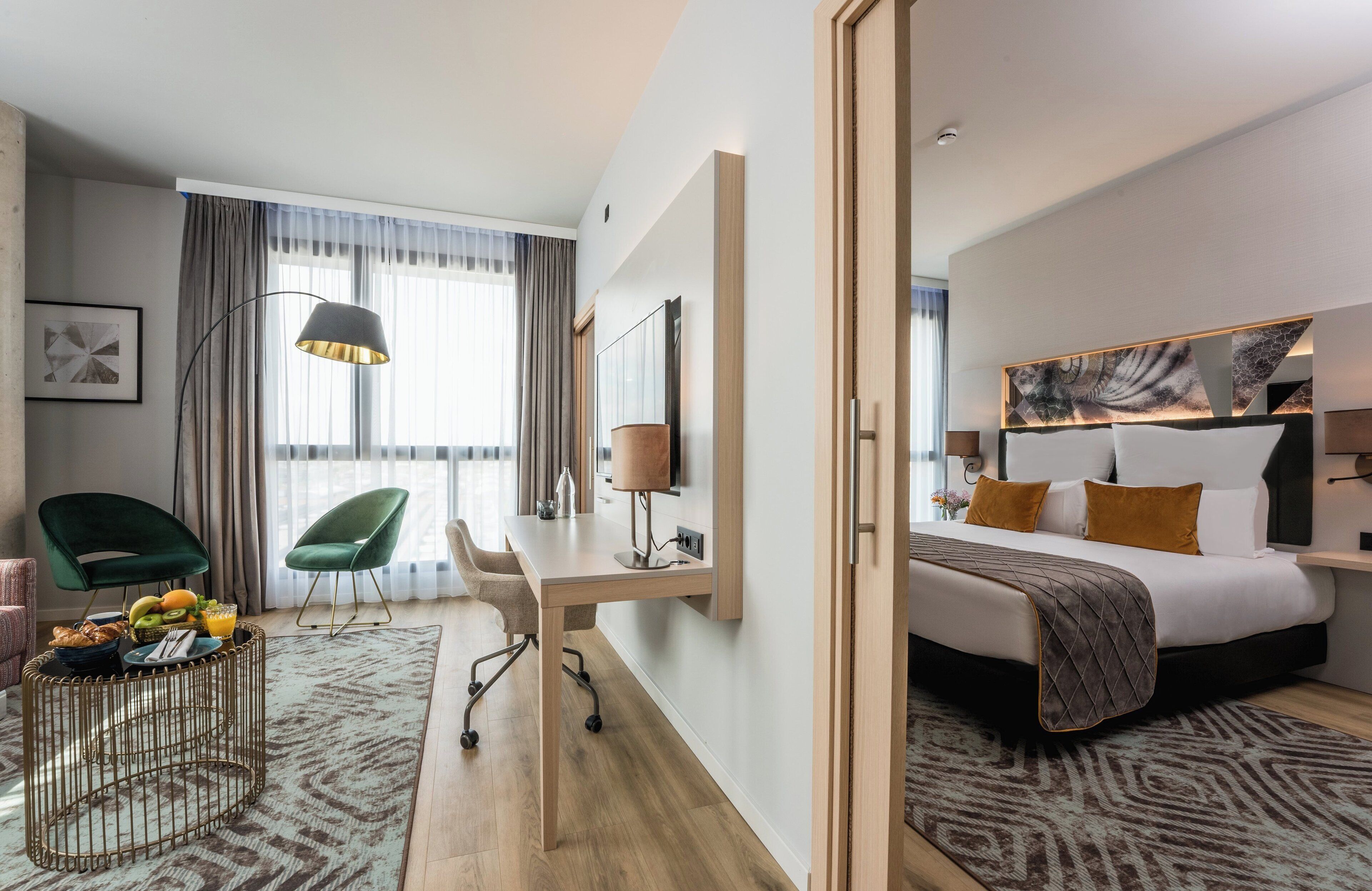 Hotelkamer met een bed, bureau, stoelen en een zithoek met fruit en een lamp.