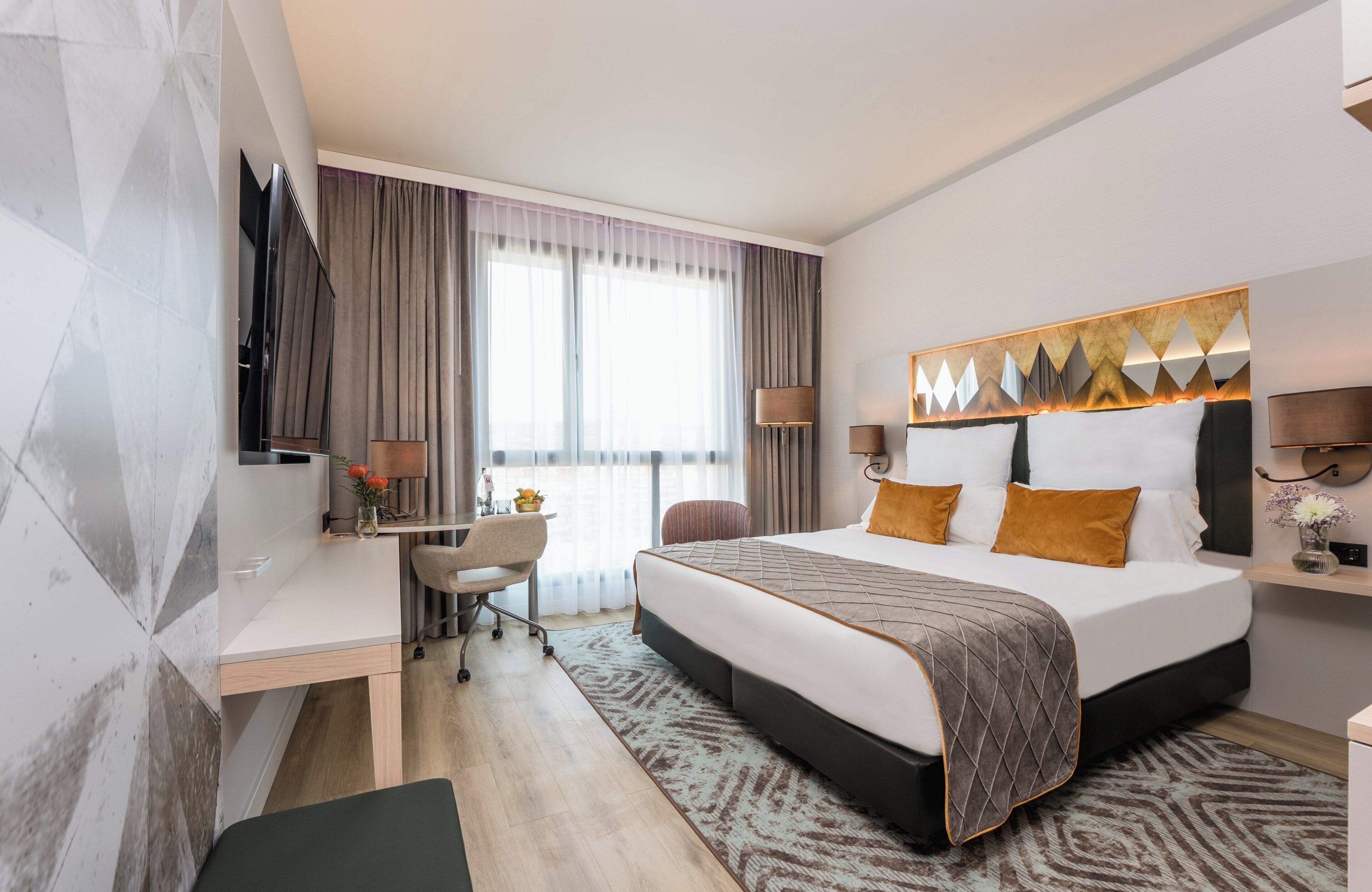 Una habitación de hotel moderna con una cama grande, un escritorio y una televisión.