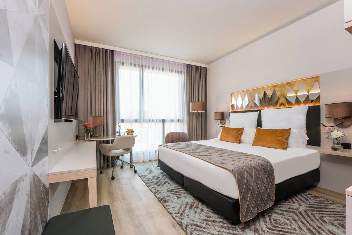 A modern hotel room with a large bed, a desk, and a TV.