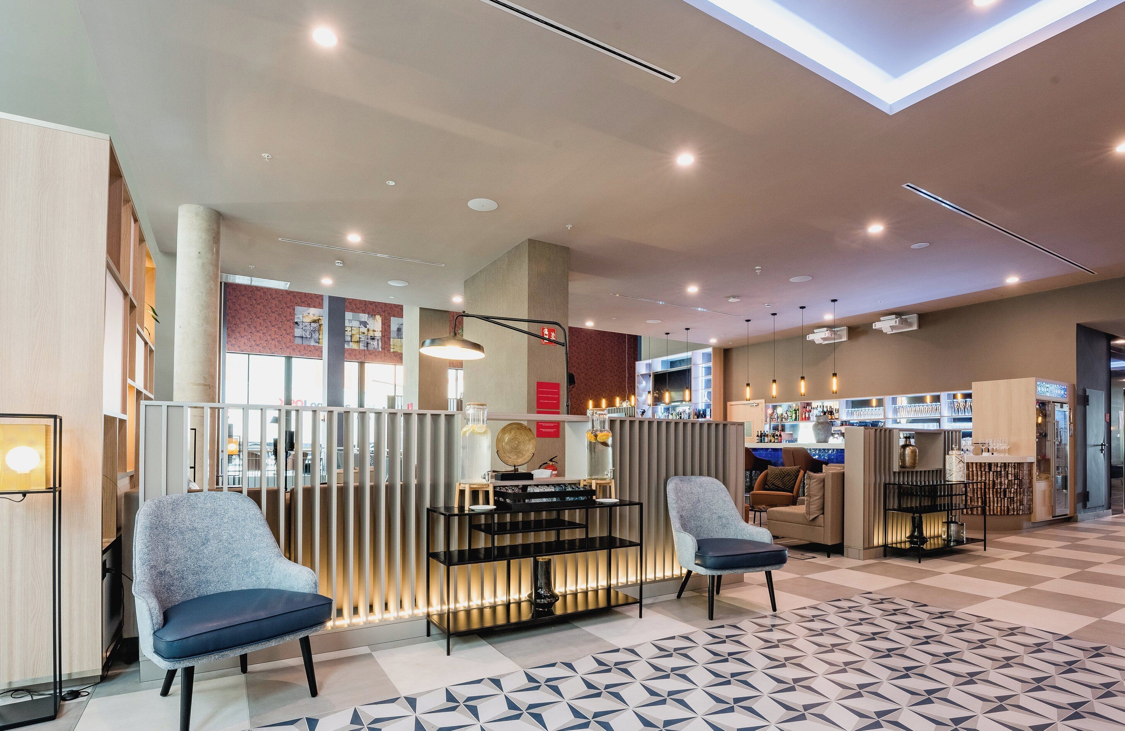 A modern hotel lobby with a reception desk, seating area, and bar.