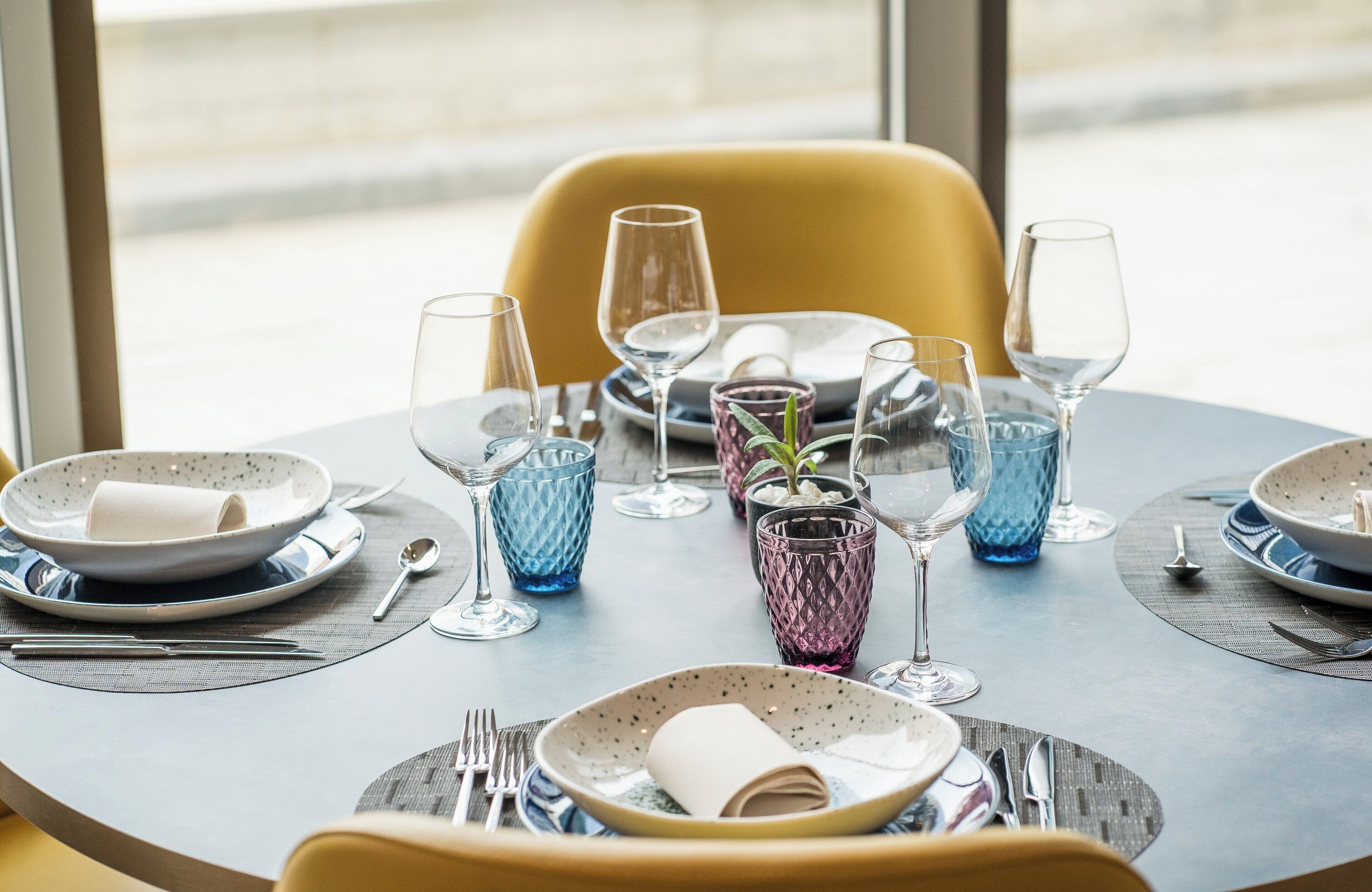 A dining table set with plates, glasses, and cutlery, with a chair visible in the background.