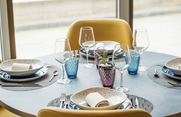 A dining table set with plates, glasses, and cutlery, with a chair visible in the background.