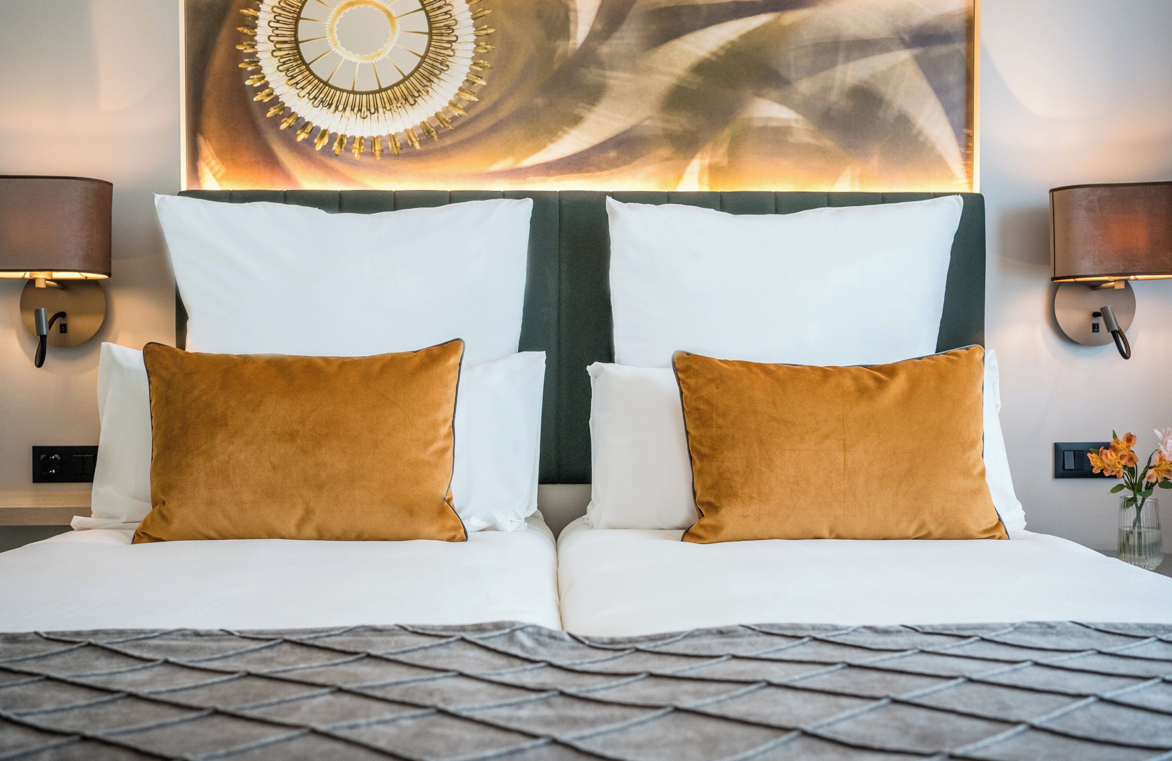 A double bed with white and mustard pillows, a green upholstered headboard, and a patterned bedspread.
