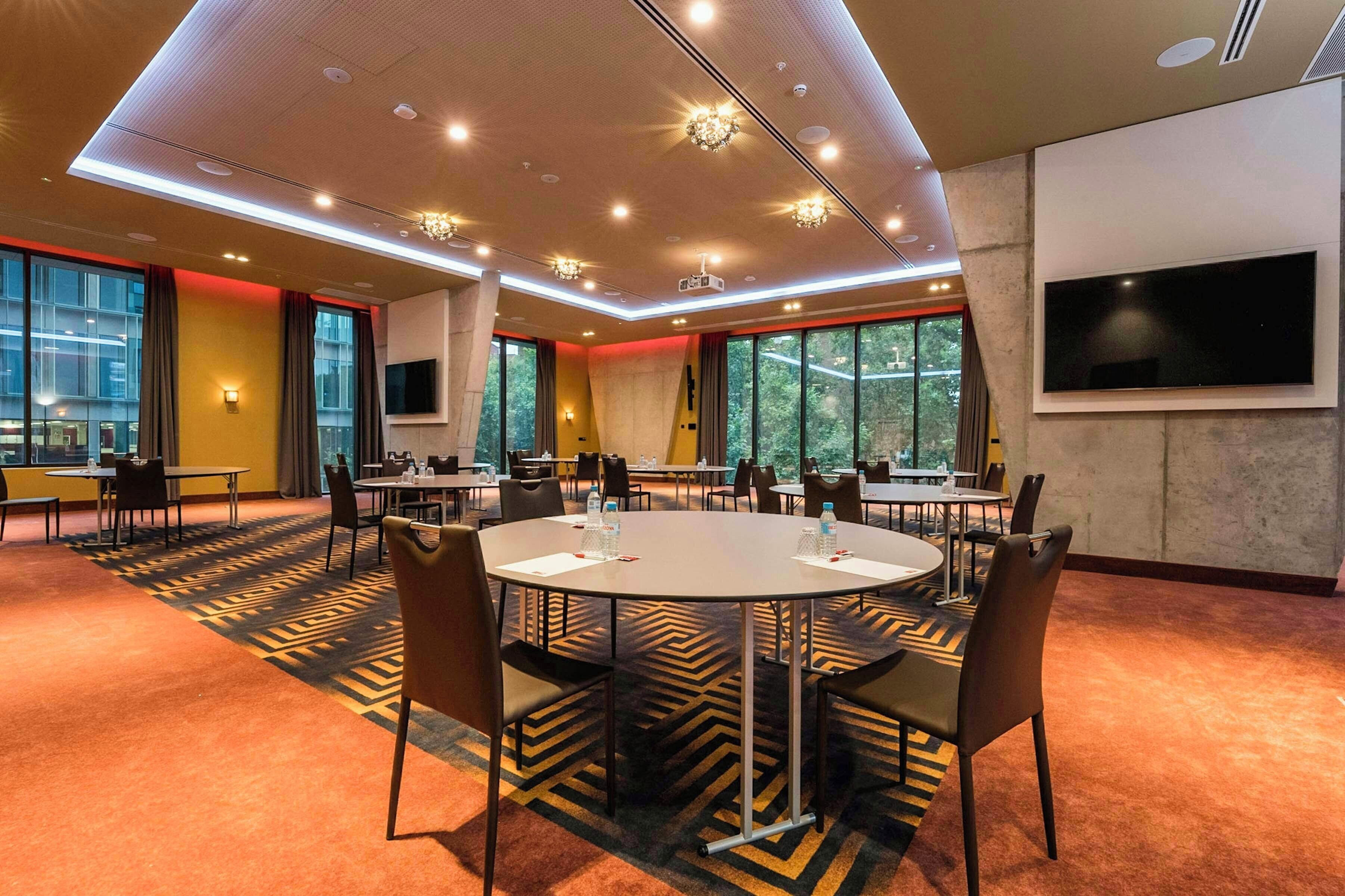 A conference room with round tables, chairs, and a large screen.