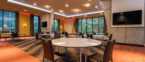 A conference room with round tables, chairs, and a large screen.