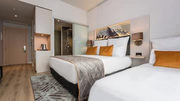 A hotel room with two beds, a large mirror, a coffee machine, and a shower area.