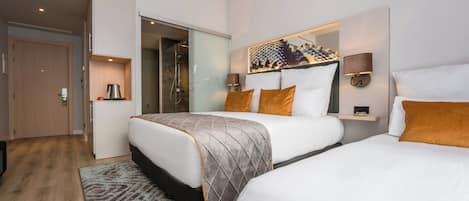 Habitación de hotel con dos camas, un espejo grande, cafetera y zona de ducha.