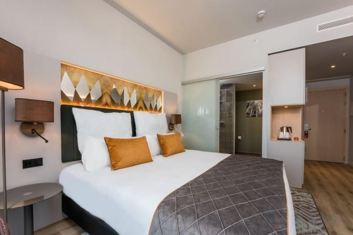 A hotel room with a large bed, a bedside table, a lamp, and a wall-mounted artwork.