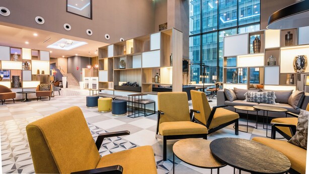 Eine geräumige Lobby mit moderner Möblierung, einer Treppe und großen Fenstern mit Blick auf die Stadt.