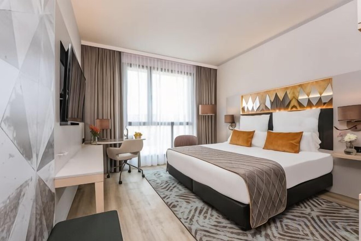 Une chambre d’hôtel moderne avec un grand lit, un bureau, une chaise, une télévision et une fenêtre avec des rideaux.