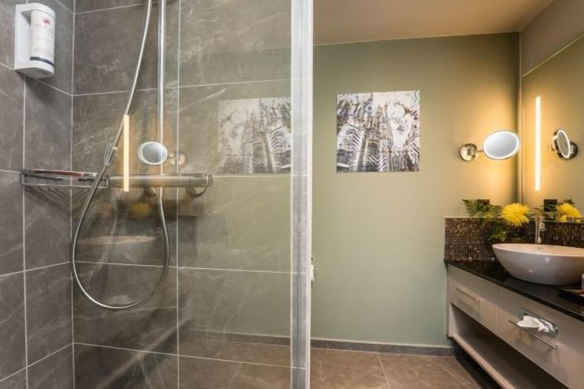 Een moderne badkamer met een douchecabine van glas, een grote spiegel en een wastafel met een bloevas.