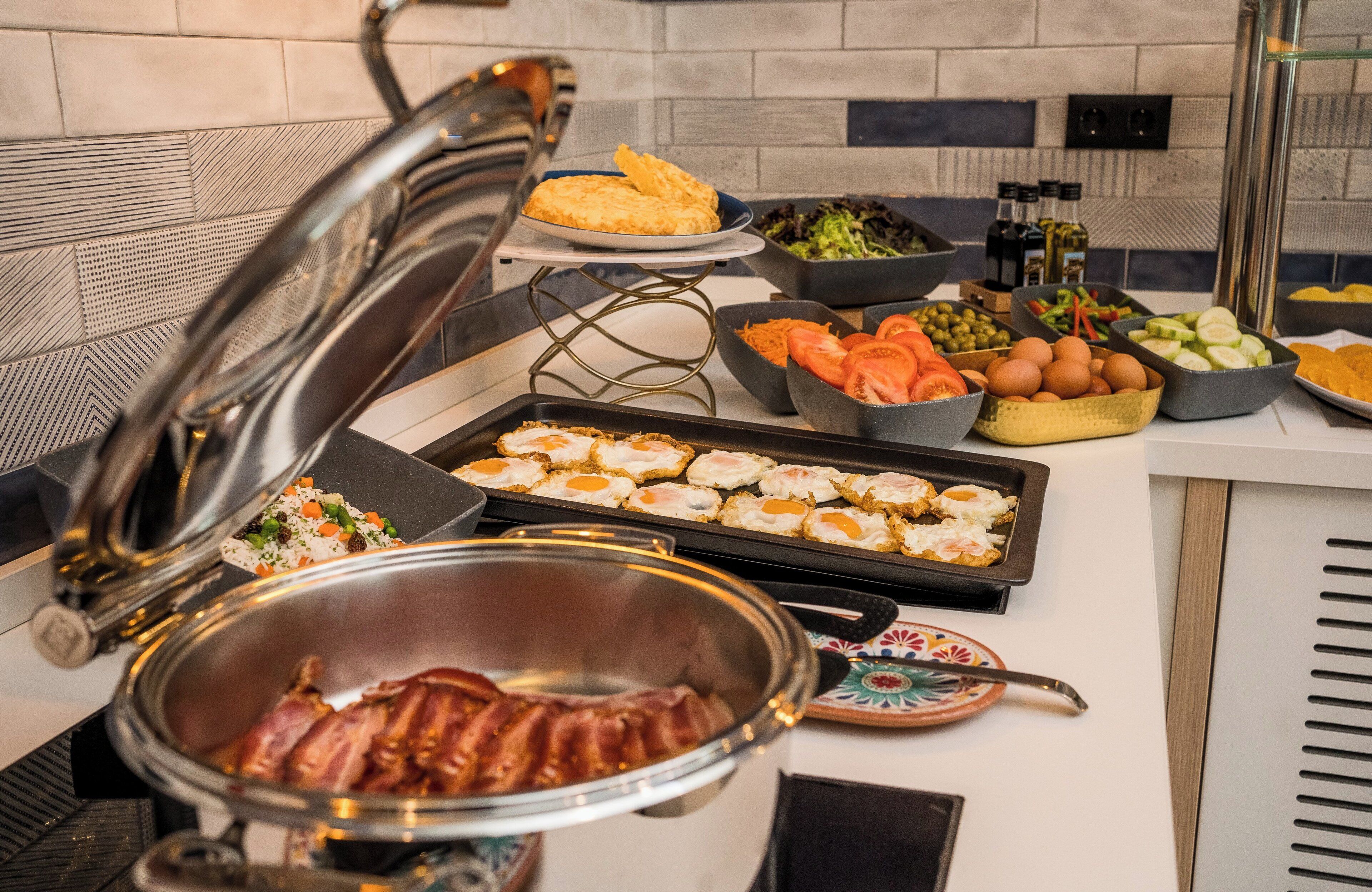 Un aparador de buffet amb diferents plats, incloent ous, bacon, verdures i amanides.