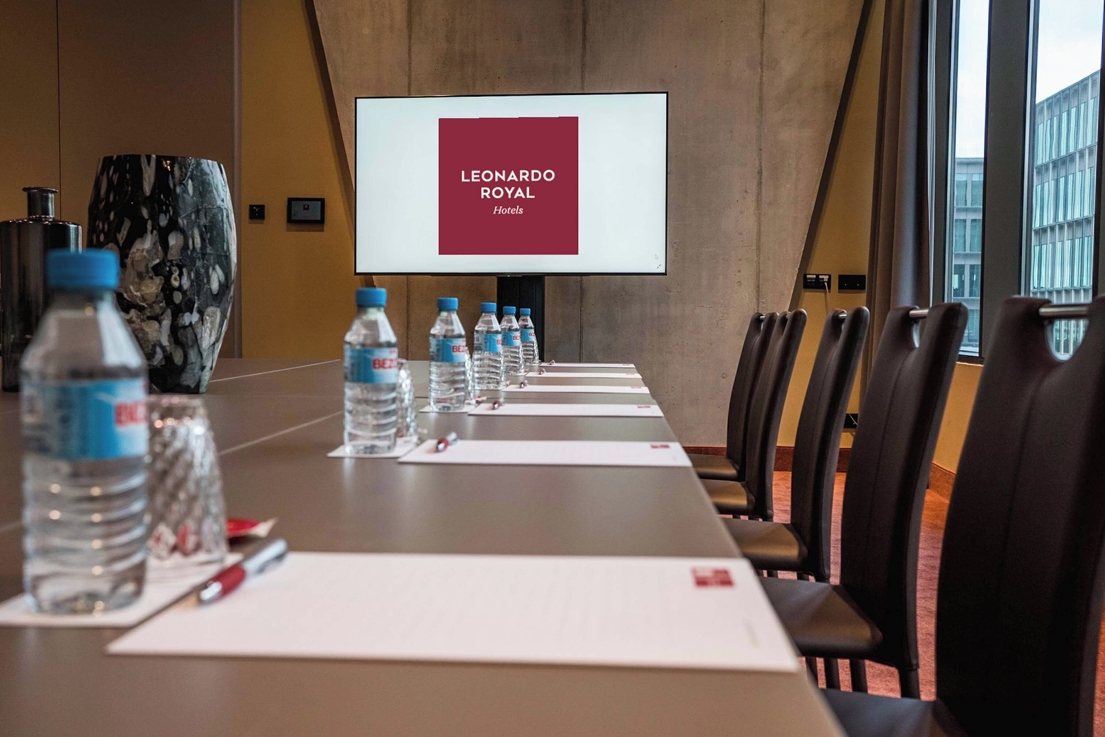 A conference room with a long table, water bottles, and a screen displaying "LEONARDO ROYAL Hotels".