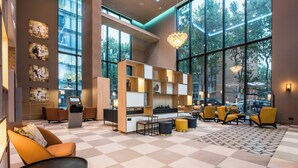 Eine großzügige Lobby mit Schachbrettmuster-Bodenbelag, modernen Sitzgelegenheiten, einem Empfangsbereich und großen Fenstern mit Blick ins Freie.