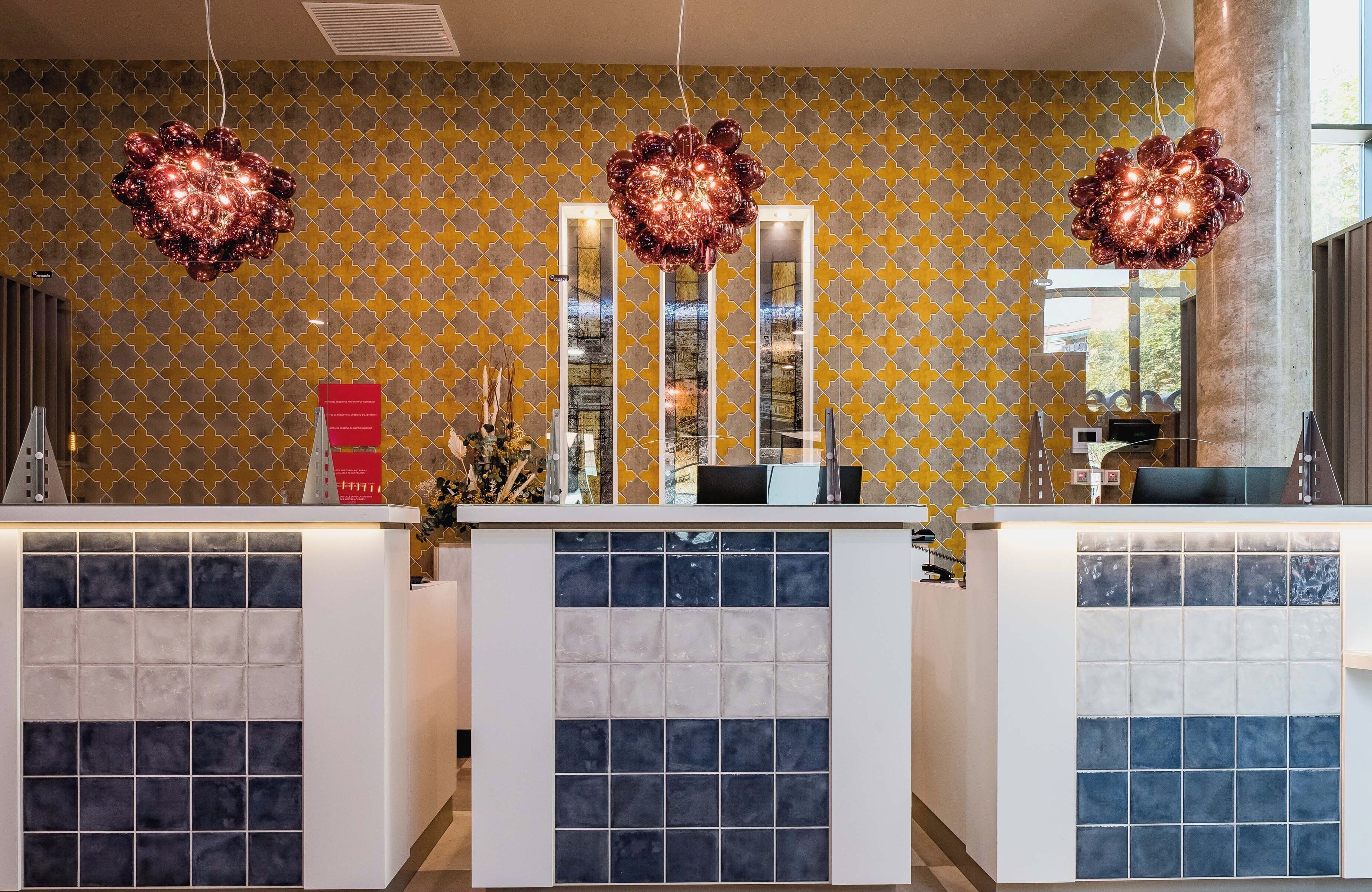 A reception area with patterned wallpaper, two large decorative light fixtures, and a counter with a tiled design.