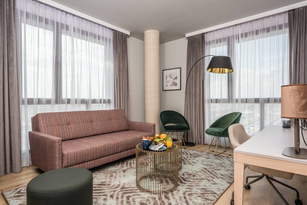 Un salon comprenant un canapé, deux fauteuils, une table basse avec des fruits, une lampe et un bureau.
