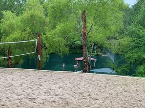 A sandy beach area with a volleyball net, a small pavilion, and a body of water surrounded by trees. - West Wing at the Manor w/ Swimming Pond & Sand Volleyball Access (Montgomery)