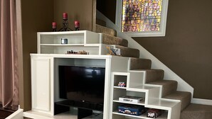 A living room with a fireplace, a television, and a staircase leading to another level. - West Wing at the Manor w/ Swimming Pond & Sand Volleyball Access (Montgomery)