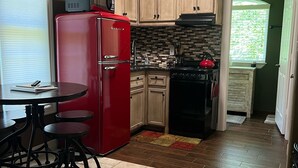 A compact kitchen with a red refrigerator, wooden cabinets, a tiled backsplash, and a small dining area with stools. - West Wing at the Manor w/ Swimming Pond & Sand Volleyball Access (Montgomery)