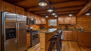 A modern kitchen with wooden cabinets, stainless steel appliances, and a bar area. - Majestic Wyoming Landscape. Riverfront log cabin. Relax in or explore out! (Meeteetse)