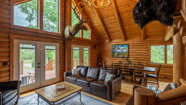 A log cabin interior with a leather sofa, dining table, and a mounted deer head. - Majestic Wyoming Landscape. Riverfront log cabin. Relax in or explore out! (Meeteetse)