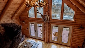 A log cabin interior with a large deer head mounted on the wall, wooden floors, and a ceiling with a chandelier made of antlers. - Majestic Wyoming Landscape. Riverfront log cabin. Relax in or explore out! (Meeteetse)