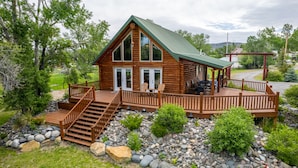 A log cabin with a deck, outdoor seating, and a stone pathway leading to the entrance. - Majestic Wyoming Landscape. Riverfront log cabin. Relax in or explore out! (Meeteetse)