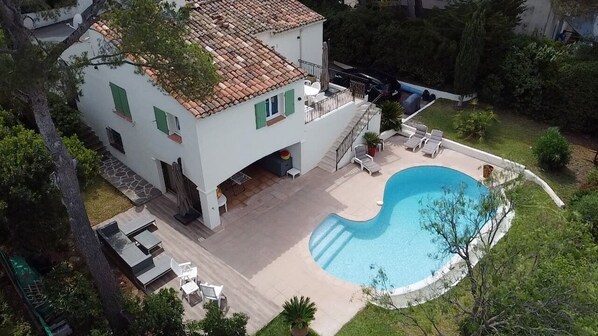 A two-story house with a swimming pool, outdoor furniture, and a garden.