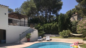 Piscina com água azul cristalina, cercada por um prédio branco com varanda, escada e rede.