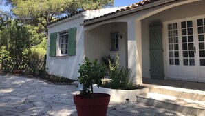 Uma casa com telhado de telhas, paredes brancas, persianas verdes e porta frontal com painéis de vidro.