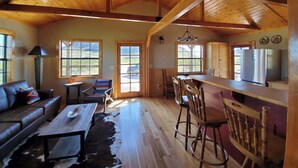 Amplia sala de estar con techo de madera, un sofá, una mesa de comedor y una zona de cocina con refrigerador.