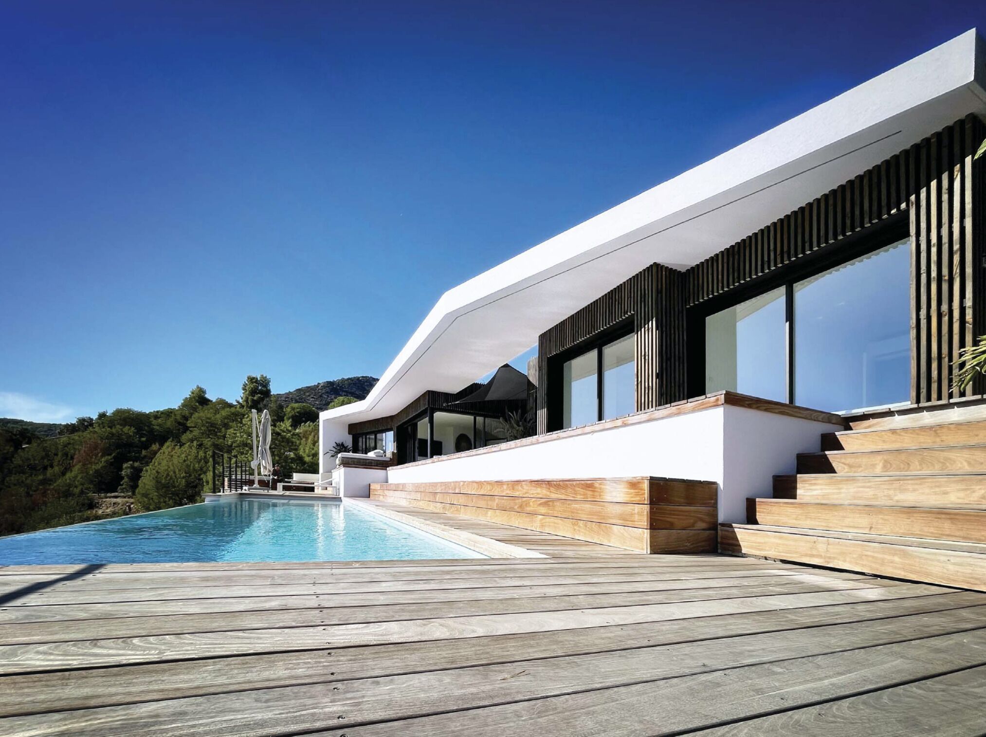 Een modern huis met een zwembad, houten terras en uitzicht op de omliggende heuvels.