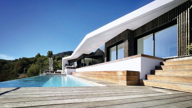 Une maison moderne dotée d’une piscine, d’une terrasse en bois et offrant une vue sur les collines environnantes.