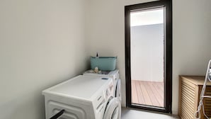 Une petite buanderie comprenant un lave-linge, un sèche-linge et une petite table sur laquelle se trouvent une bouteille et un récipient.