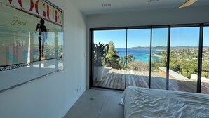 Une chambre dotée d’une grande fenêtre donnant sur la mer et sur le paysage urbain.