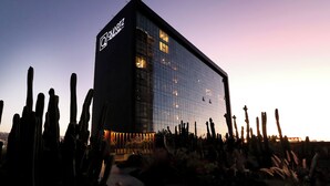 Un hotel moderno con fachada de vidrio y un jardín desértico con cactus.