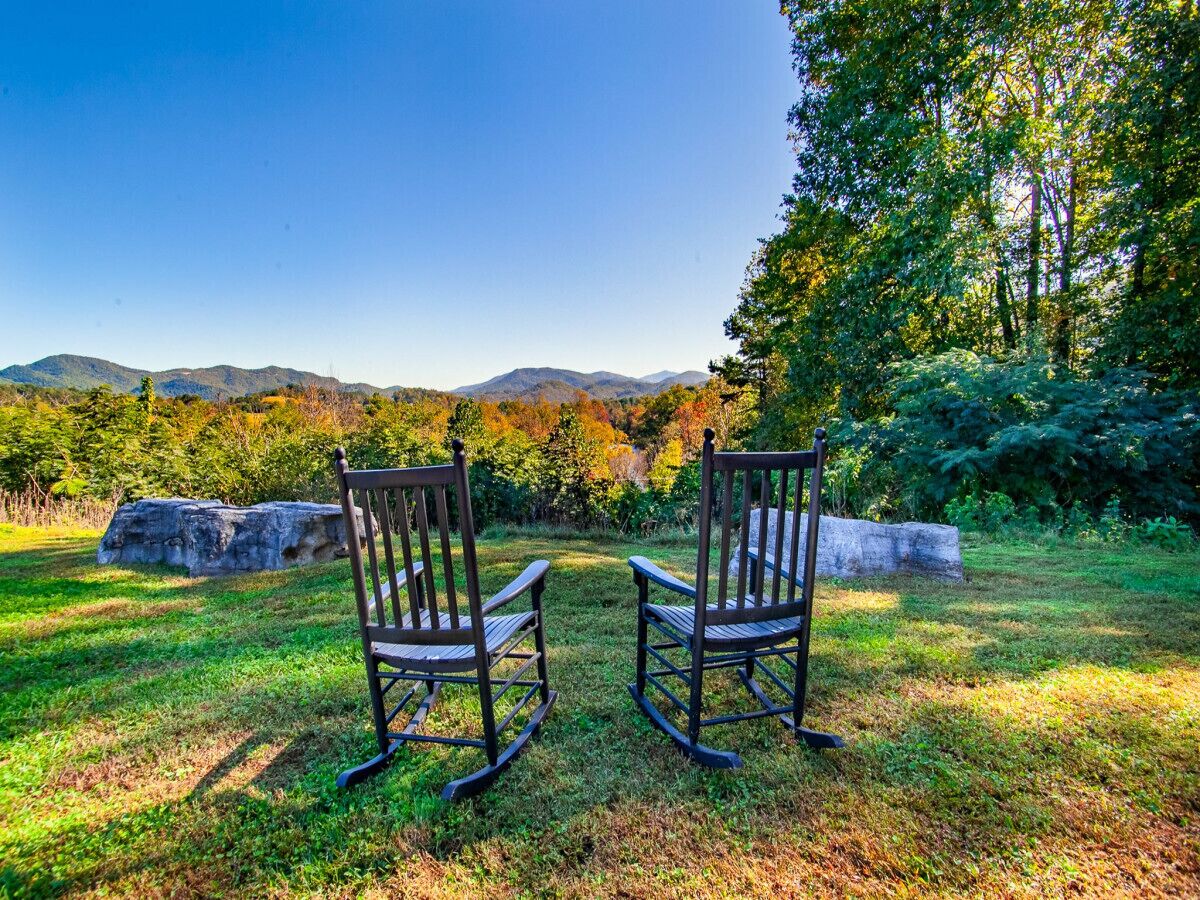 Two rocking chairs in a grassy area with a view of mountains and trees.