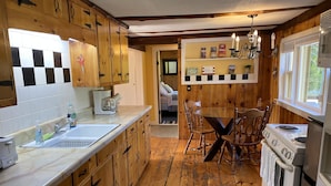 A rustic kitchen with wooden cabinets, a marble countertop, a dining table with chairs, and a stove.