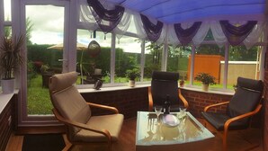 A conservatory with a glass table and two chairs, a view of the garden, and a brick wall. - Yorkshire Wolds Spacious Modern Holiday Bungalow (Driffield)