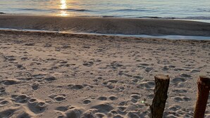 En strand med fodaftryk, der fører hen til vandet, en træpæl og en båd i det fjerne.