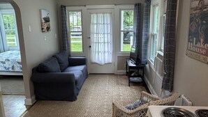 En stue med sofa, spiseplads med bord og stole, et køkken med komfur, samt udsigt til det fri.